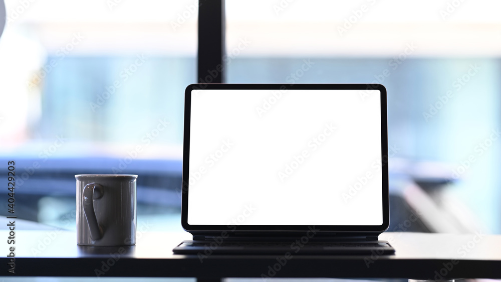Poster front view of mock up tablet computer with blank screen and coffee cup on wooden table.