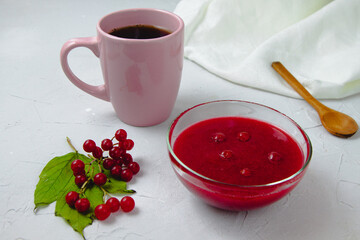Autumn composition with viburnum jam, viburnum branches and leaves, white linen towel, pink cup, and wooden spoon. Concept of breakfast