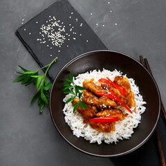 Chicken baked in sauce served with rice and vegetables on gray background.