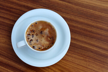 Cup of cappuccino coffee in a white saucer on wooden table, top view