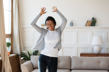 Happy laughing young african american biracial woman dancing to energetic disco music in modern living room, enjoying carefree domestic hobby activity, celebrating freedom on weekend alone indoors. - Powered by Adobe