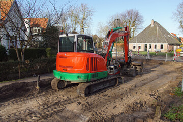 Fototapeta na wymiar Roadwork with a red, green excavator in the Dutch village of Bergen. Netherlands, January 