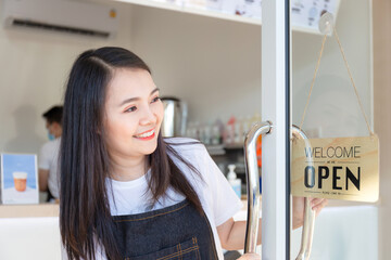 Young girl wearing an apron. Happy girl opening on the doors at a cafe and looking at open sign wood board