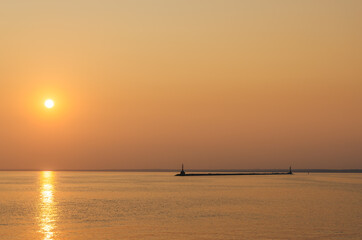 A lighthouse against the sunset sky. Beautiful peaceful seascape. Small ships on the sea horizon.