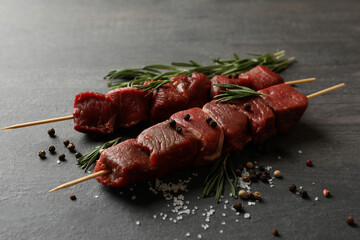Skewers with raw meat and spices on dark background