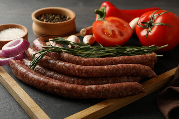 Board with raw sausages, herbs and spices on dark background