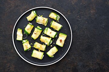 Roasted zucchini rolls stuffed with cream cheese and nuts on a black plate on a dark concrete...