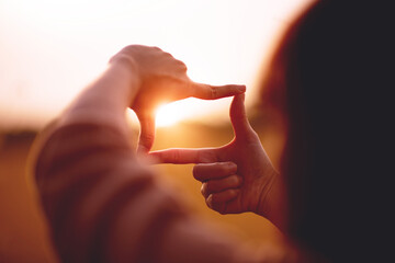 New year planning and vision concept, Close up of woman hands making frame gesture with sunset, Female capturing the sunrise. copy space. - obrazy, fototapety, plakaty