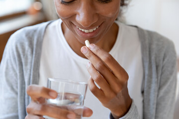 Close up happy young african american young woman taking daily dose of complex healthcare skin,...