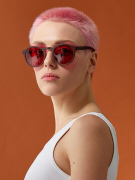 Hipster pinkhead girl in red sunglasses on brown background.