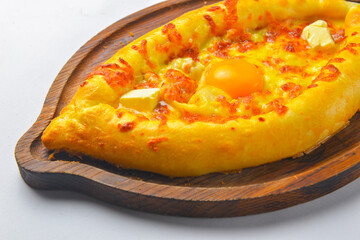 Khachapuri with cheese and egg on a wooden board over white background. Georgian cuisine concept.