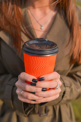 Young attractive woman with a cup of coffee to go. Drinking coffee outside in autumn clothes during fall season.