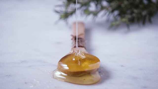Flow of honey. Golden, yellow, raw honey is dropping from honey dipper on wood tablespoon. Healthy sweet ingredient for natural cosmetics, pastry and breakfast.