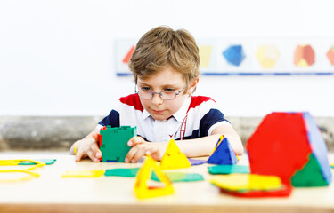 Happy kid boy with glasses having fun with building and creating geometric figures, learning mathematics and geometry