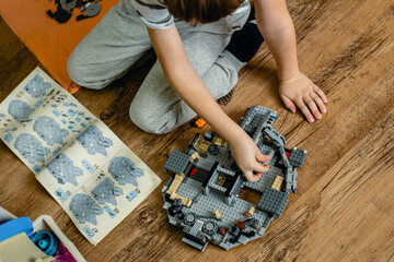 Naklejka premium A blond boy of nine years old collects a large Lego set of the Millennium Falcon in his room. Based on the film Star Wars.
