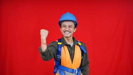 Handsome asian worker man wearing uniform, helmet, safety harness over isolated red background celebrating surprised and amazed for success with arms raised and open eyes. Winner concept