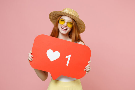 Young smiling redhead ginger bcaucasian blogger woman 20s wear straw hat glasses summer clothes hold huge like sign from social network heart form isolated on pastel pink background studio portrait