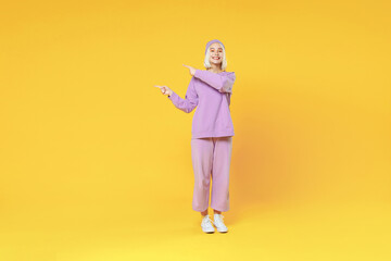 Full length of young caucasian woman 20s bob haircut wearing casual basic purple suit beanie hat pointing index fingers aside on workplace looking away isolated on yellow background studio portrait.