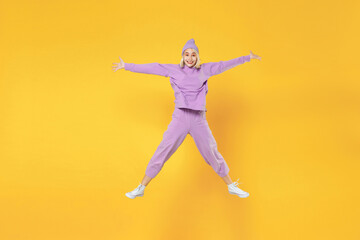Fototapeta na wymiar Full length of young overjoyed caucasian excited fun woman 20s bob haircut in casual basic purple suit beanie hat high jumping up with speading hands isolated on yellow background studio portrait.