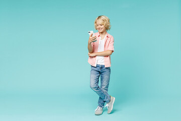 Full length of smiling little kid boy 10s in pink shirt using mobile cell phone typing sms message...