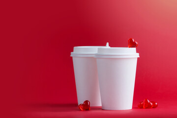 Two white cups for coffee and tea stand next to glass hearts on a red background. Mockup. Horizontal format. Copyspace