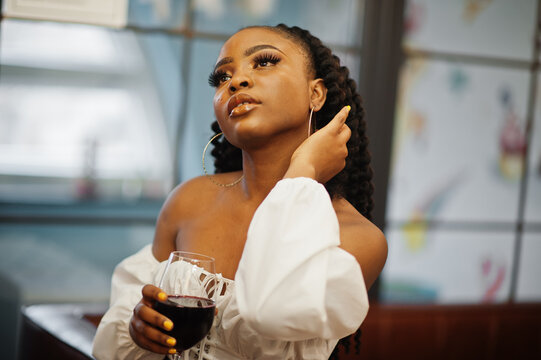 Beautiful African American Woman In White Blouse And Red Leather Pants Pose At Restaurant With Glass Of Wine.