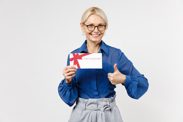 Blonde employee business woman 40s wearing blue classic shirt glasses formal clothes hold gift voucher flyer mock up show thumb up gesture isolated on white background studio portrait. Wealth concept