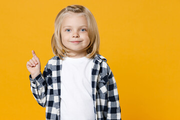 Little fun happy kid boy 4-5 years old wearing casual clothes pointing on workspace area isolated on bright yellow wall color background children studio portrait. People childhood lifestyle concept.