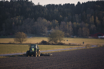 Fototapeta premium Tractor farmer plowing field ploughing soil farming dust agriculture sunset