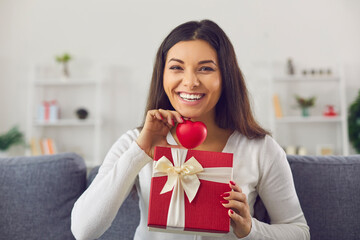 Skype conference headshot happy smiling young woman in love sitting on sofa at home, holding red...