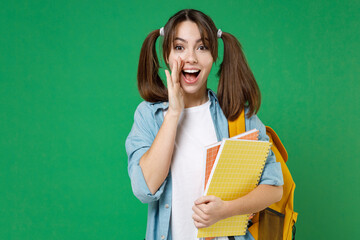 Excited young woman student in basic blue shirt backpack hold notebooks scream news with hands near mouth isolated on green wall background studio. Education in high school university college concept.