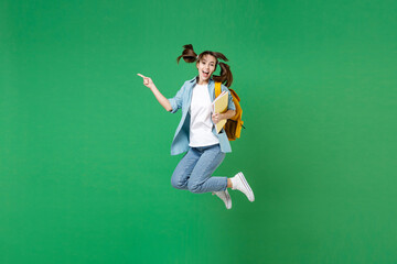 Full length excited young woman student in shirt backpack hold notebooks jumping point finger aside isolated on green background studio portrait. Education in high school university college concept.