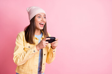 Portrait of beautiful young lady playing games gamepad in hands open mouth wear cap isolated on pink color background © deagreez