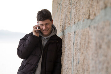 smiling man using smart phone on stone wall