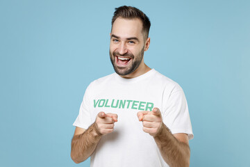 Cheerful young bearded man 20s in white volunteer t-shirt pointing index fingers on camera isolated...