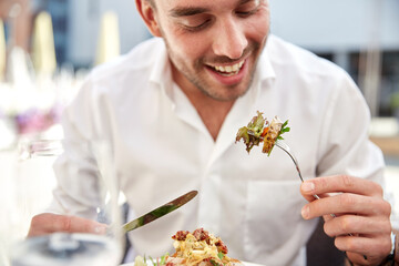people, food and leisure concept - close up of happy smiling man with fork and knife eating dinner at restaurant terrace