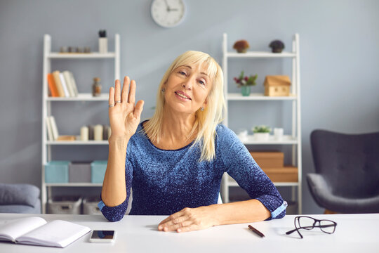 Adult female teacher waves her hand in greeting her students in an online lesson during isolation and quarantine. Woman conducts online training from home. Concept of distance learning.