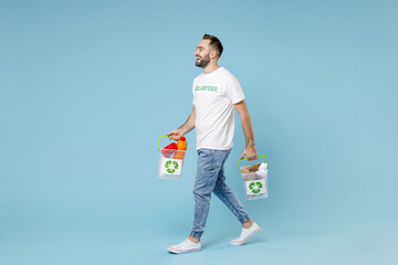 Fototapeta na wymiar Full length side view of funny young man in volunteer t-shirt hold baskets with plastic paper trash isolated on blue background studio. Voluntary free assistance help trash sorting recycling concept.