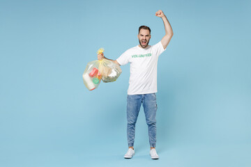 Full length of angry young man in volunteer t-shirt hold bags with plastic paper trash clenching fist swearing isolated on blue background. Voluntary free assistance trash sorting recycling concept.