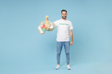 Full length smiling young man in white volunteer t-shirt hold bags with plastic paper trash...