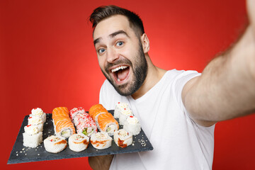 Close up of excited young man in white t-shirt doing selfie shot on mobile phone hold makizushi...