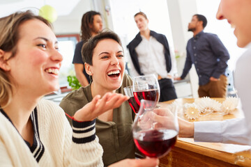 Lachende Frauen als Freundinnen haben Spaß auf Party bei Glas Wein in der Küche