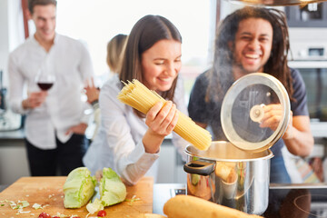 Lachende Freunde am Herd in Küche beim Nudeln kochen