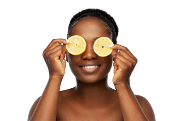 beauty, skin care and detox concept - beautiful african american woman making eye mask of lemons...