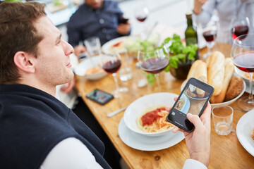 Mann nutzt Smartphone beim gemeinsamen Essen mit Freunden - obrazy, fototapety, plakaty