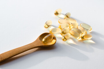 Heap of Omega 3 capsules on a white plate with a wooden spoon.