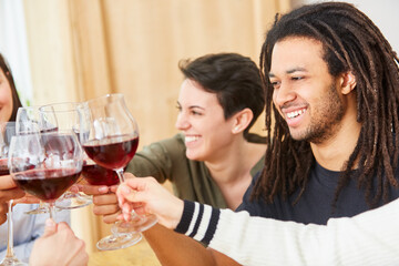 Glückliche Freunde stoßen zusammen mit Glas Rotwein bei Feier an