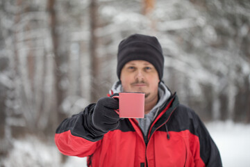 Fototapeta na wymiar A mug with a hot drink in the hands of a man. Portrait of a man for a walk in the winter forest.