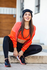 Warming up before training. Photo of sporty girl with perfect body on street background. Strength and motivation. Happy young woman in sports clothing smiling. Muscular fitness model