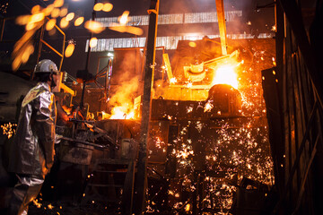 Foundry worker controlling process of melting iron in furnace. Burning liquid steel pouring and...